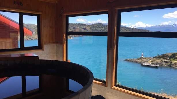 Una cabaña de madera con amplias ventanas que dan a un lago y montañas.
