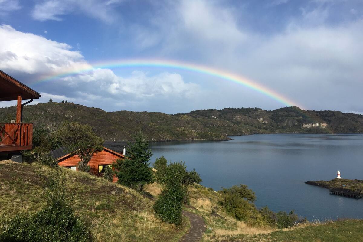 A wooden cabin with a view of a lake and a rainbow.