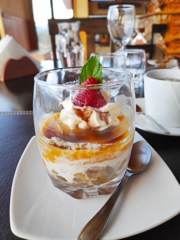 A dessert in a glass on a white plate with a spoon, set on a table with a black surface. - Patagonia Acres (Chile Chico)