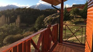 Una terraza de madera con vistas a montañas nevadas y un valle boscoso.