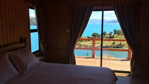 Un dormitorio con una cama grande, paredes de madera y una ventana con vistas panorámicas a un lago y montañas.