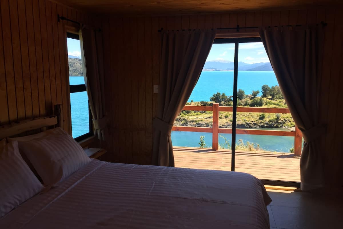 A bedroom with a large bed, wooden walls, and a window overlooking a scenic view of a lake and mountains.