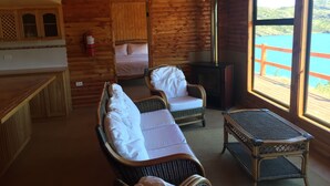 Una cabaña acogedora con una cama, dos sillas de mimbre, una mesita y vistas a un lago a través de amplias ventanas.