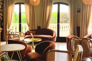 Una habitación con sofá, sillas, una mesita redonda y ventanas grandes con cortinas.