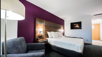 A hotel room with a bed, two armchairs, a nightstand, a lamp, and a wall-mounted picture.