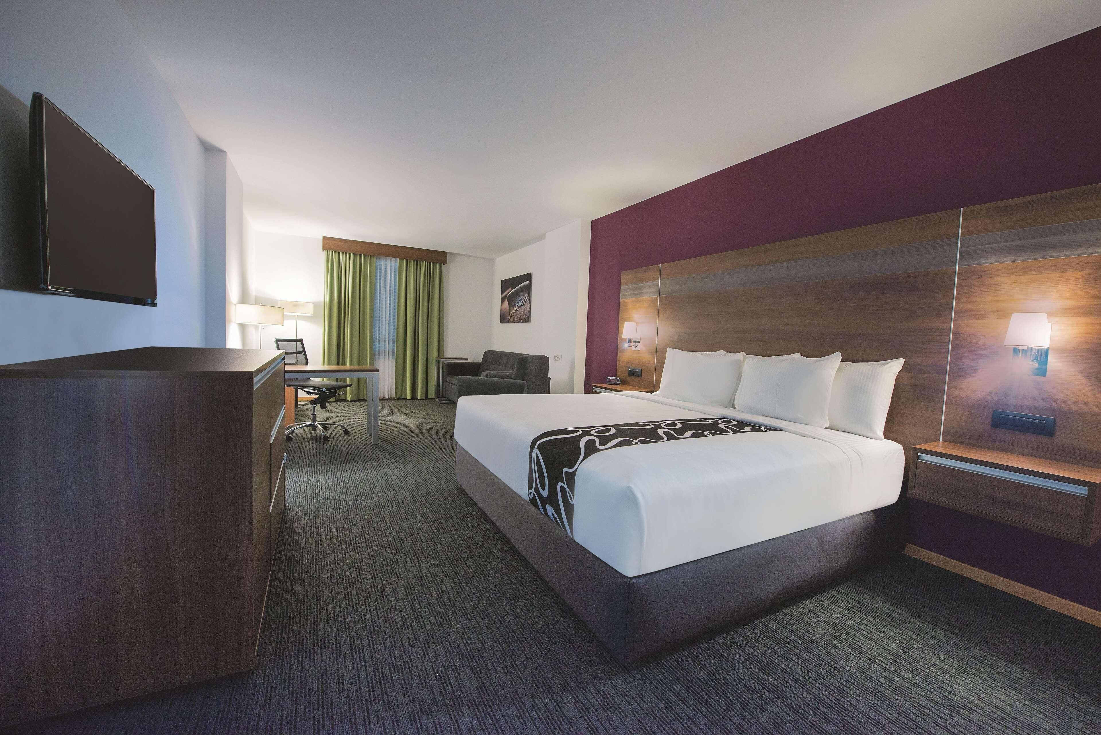 A hotel room with a large bed, a desk, a chair, a flat-screen TV, and a lamp.