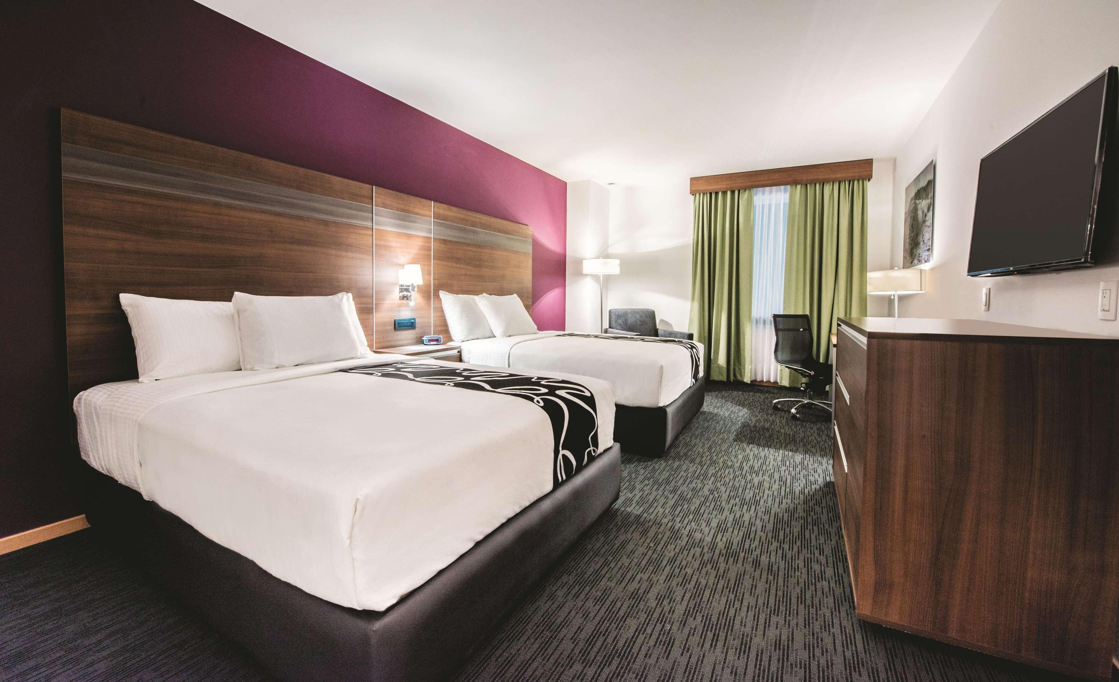 A hotel room with two beds, a desk, a chair, a TV, and a large mirror.