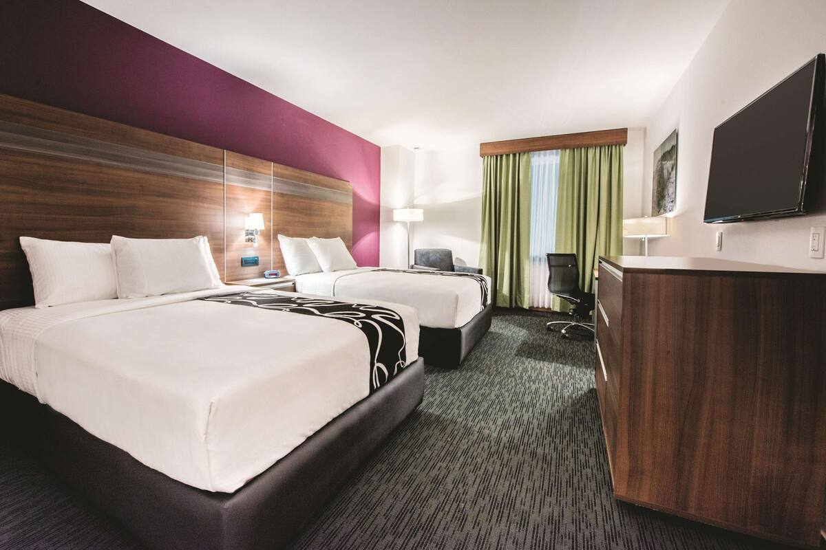 A hotel room with two beds, a desk, a chair, a flat-screen TV, and a large mirror.