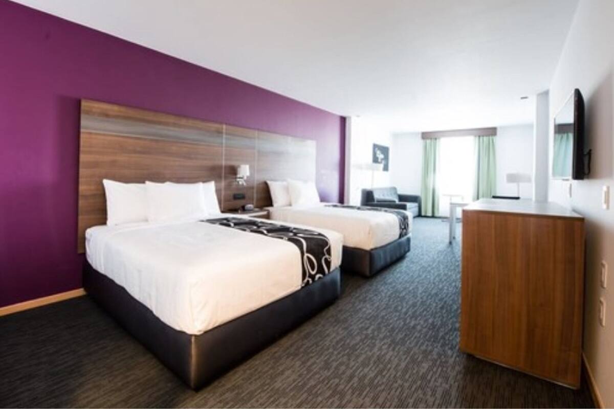 A hotel room with two beds, a wooden headboard, a desk, and a television.