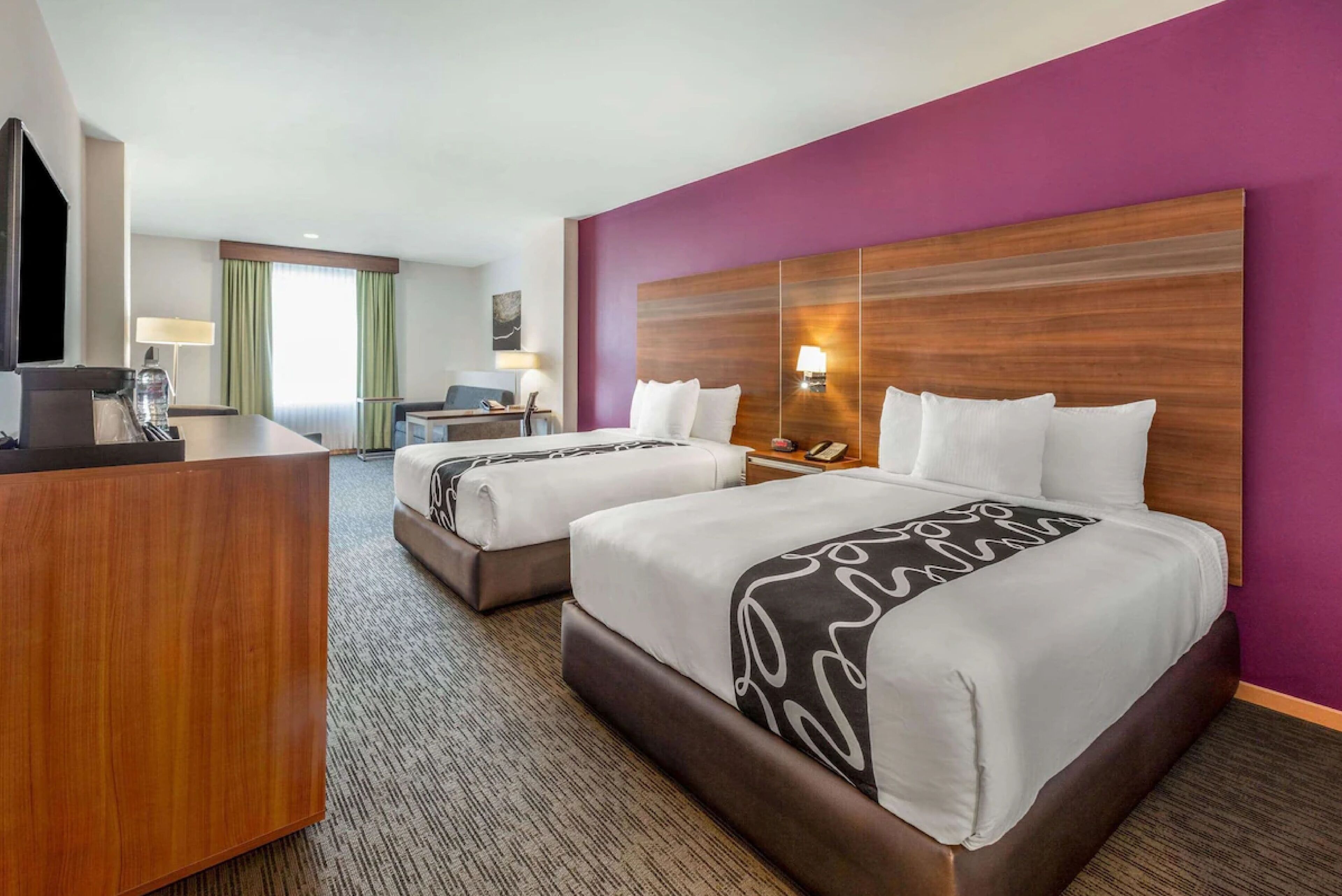 A hotel room with two beds, a desk, a TV, and a lamp.