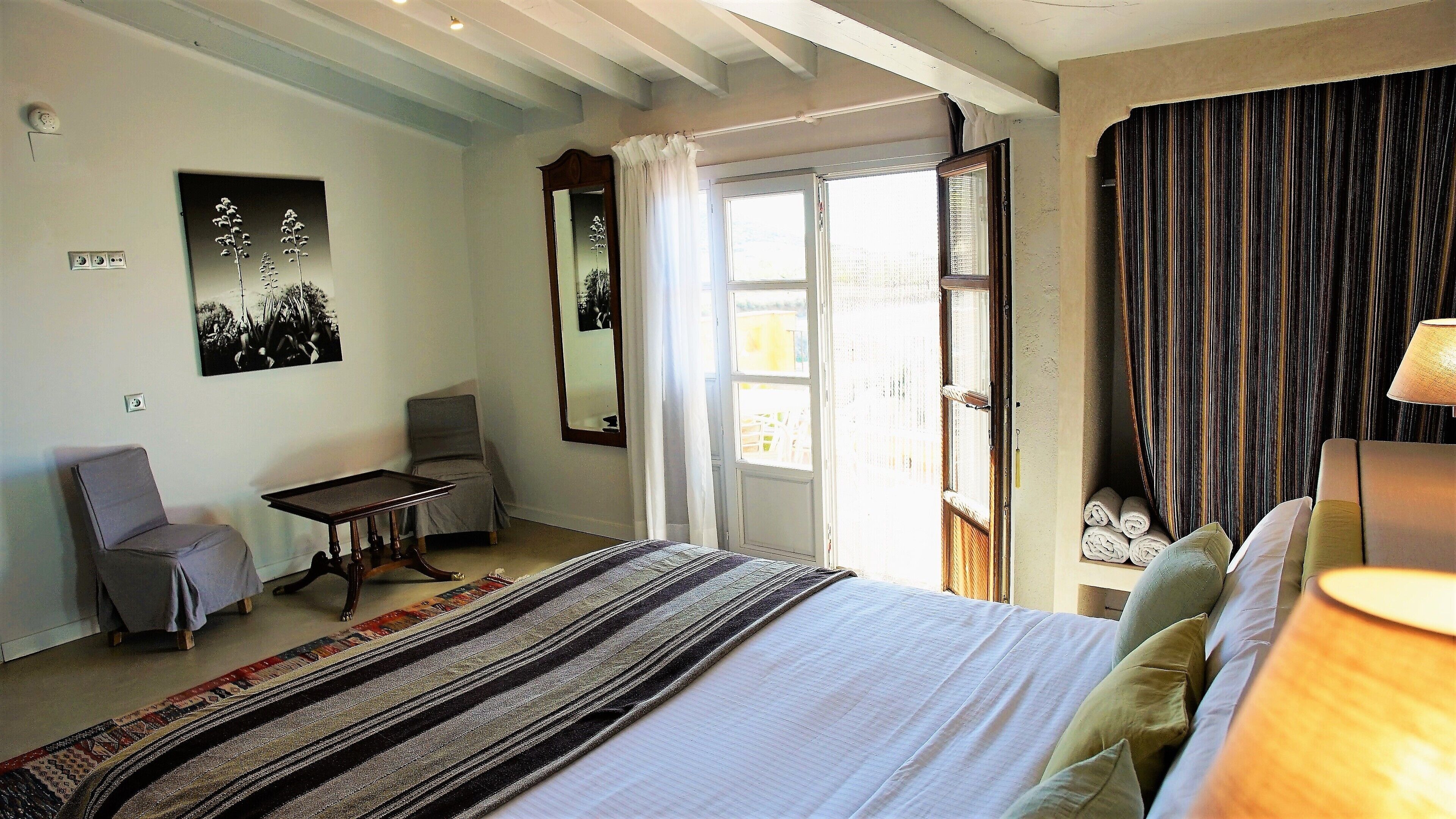 A bedroom with a bed, a chair, a small table, and a window with curtains.