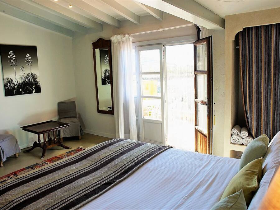 A bedroom with a bed, a chair, a small table, and a window with curtains.