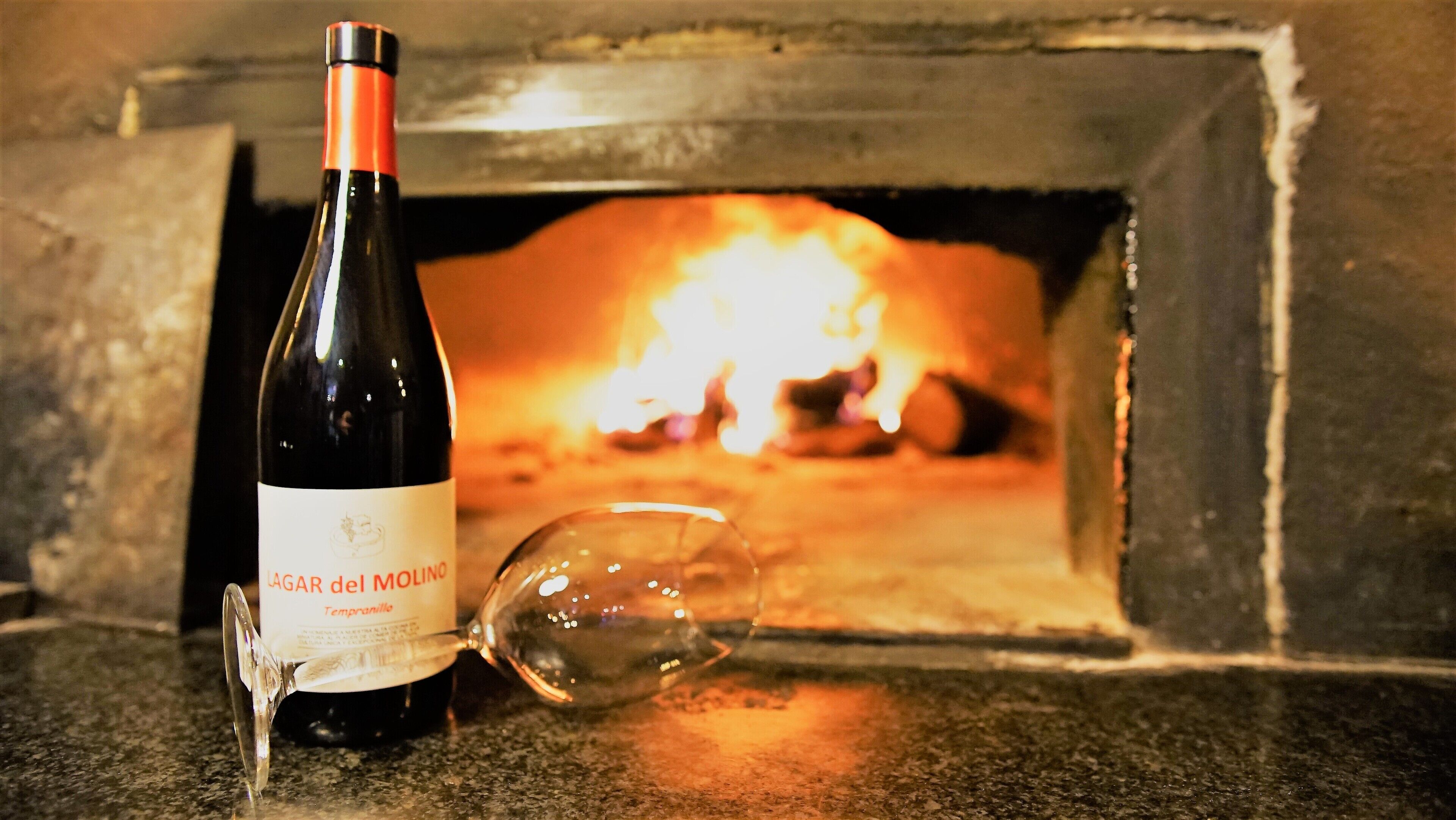 A bottle of wine and a wine glass in front of a wood-fired oven.