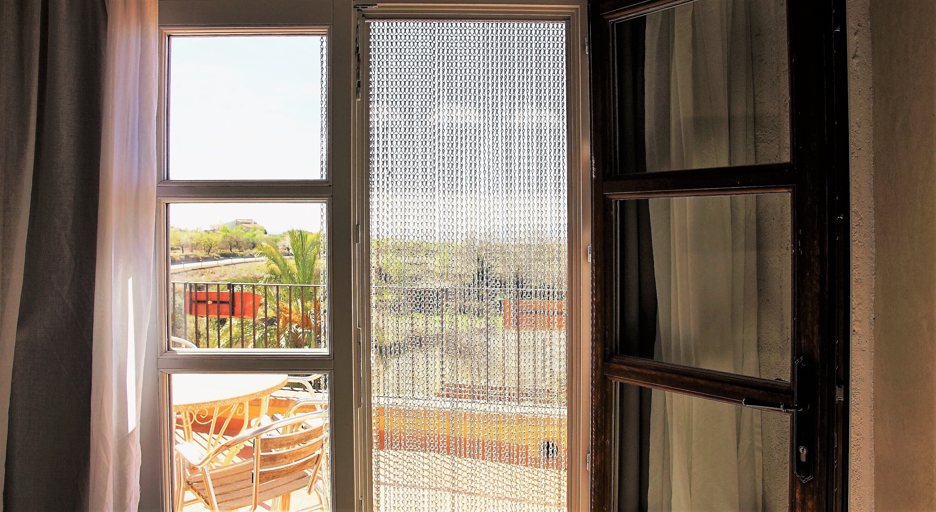 Een kamer met een groot raam, een deur en uitzicht op een balkon met stoelen en een tafel.