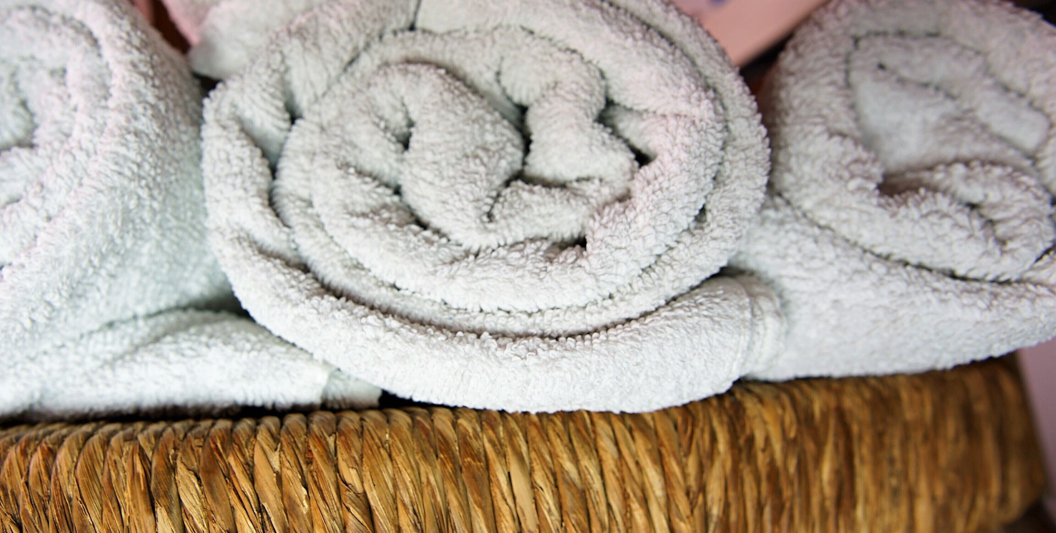 A close-up of neatly rolled white towels stacked on a woven basket.