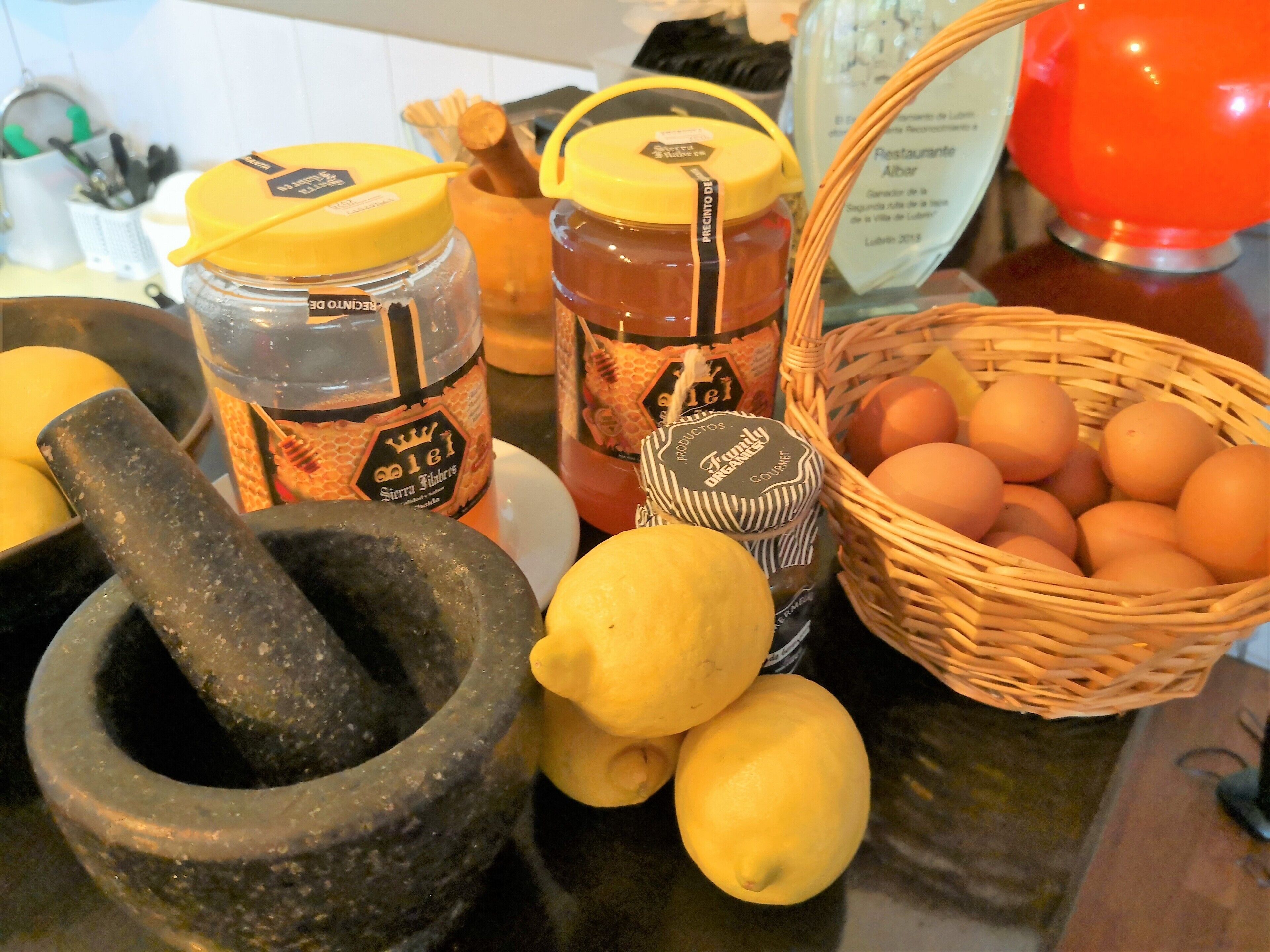 Una encimera de cocina con un mortero, limones, tarros de miel y una cesta de huevos.