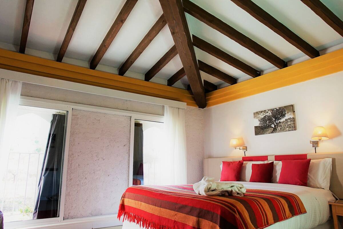 Un dormitorio con cama, dos lámparas de noche, una ventana con cortinas y un cuadro en la pared.