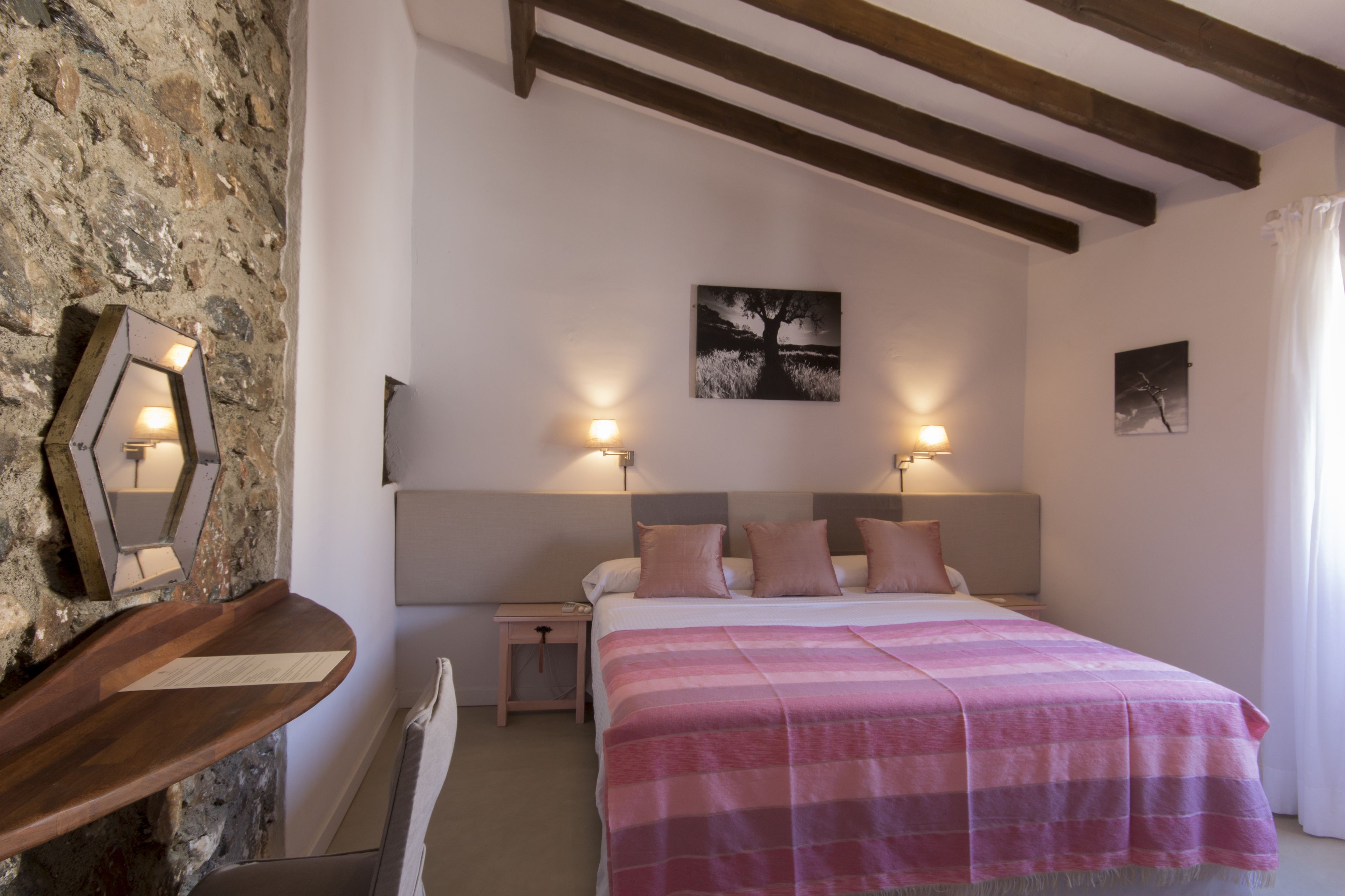 A bedroom with a bed, two bedside tables, a nightstand, a wall-mounted mirror, and a painting.
