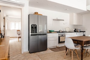 Une cuisine moderne dotée d’un réfrigérateur en acier inoxydable, de meubles blancs, d’une table à manger en bois et d’un îlot de cuisine avec des sièges.
