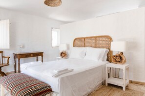Un dormitorio ordenado con una cama grande, mesitas de noche, un banco y una ventana.