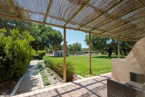 Un espacio exterior techado con un sendero pavimentado, una pérgola de madera y muebles de mimbre.