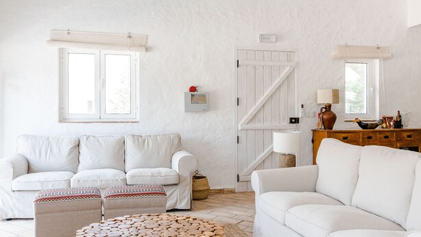 Una sala de estar moderna con un sofá blanco, una mesa de centro de madera y una puerta blanca con ventanal.