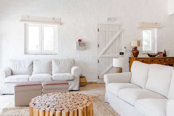 A modern living room with a white sofa set, a wooden coffee table, and a white door with a window.