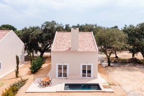 Una casa de dos pisos con techo de tejas, piscina y jardín con árboles.