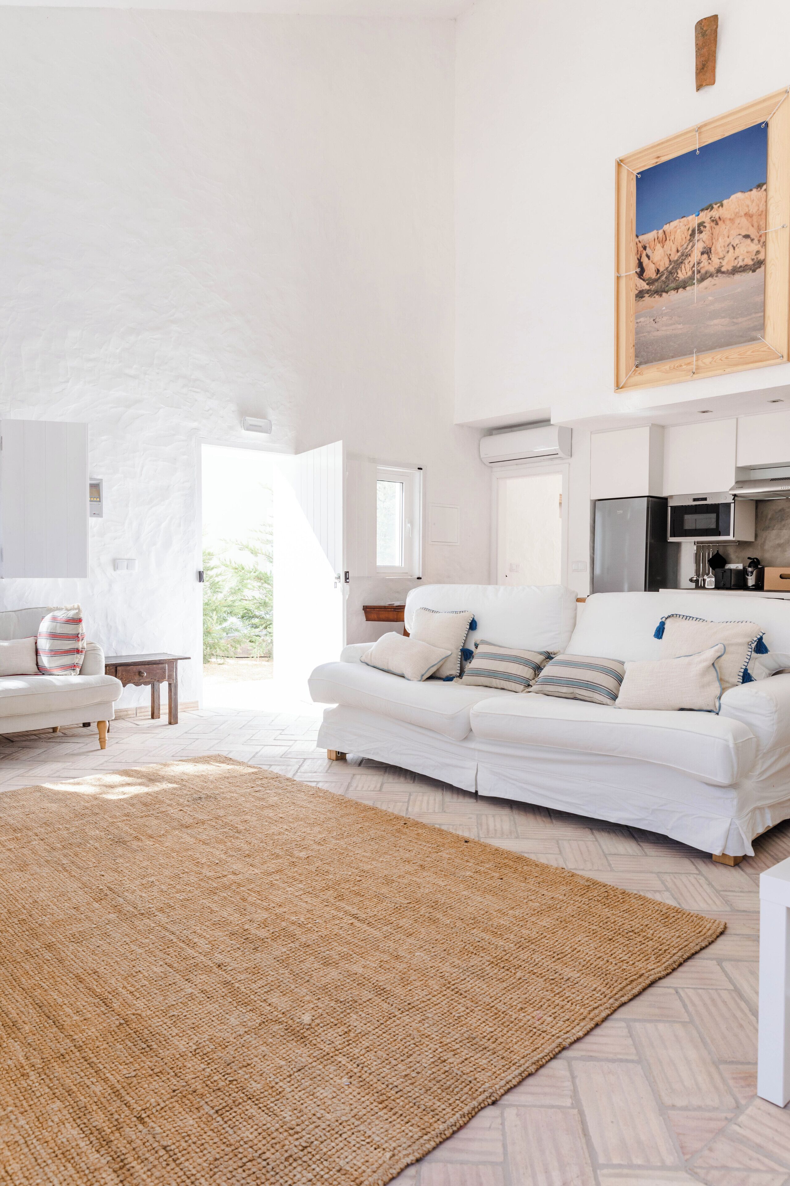Un salon spacieux avec un canapé blanc, un tapis tissé et un tableau accroché au-dessus du canapé.