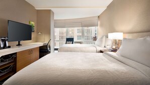 Een hotelkamer met een groot bed, een televisie, een bureau met stoel en een raam met uitzicht op gebouwen.