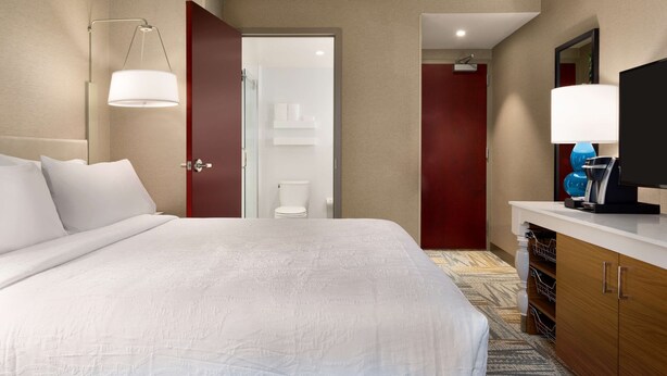 Une chambre d’hôtel avec un grand lit, un bureau avec une lampe, une télévision et une salle de bain visible à travers une porte ouverte.