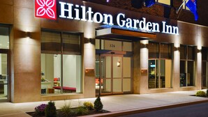 Het uiterlijk van een Hilton Garden Inn met een groot verlicht bord, een glazen ingang en een goed verlichte gevel.
