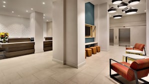 Een moderne receptie met een receptiebalie, een zithoek en een trap naar een lift.