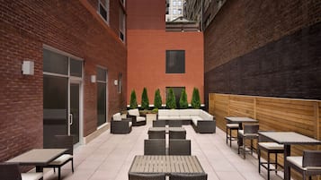 Un patio con mobiliario exterior, paredes de ladrillo y un macetero central con árboles.