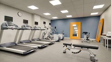 Un gimnasio con cintas de correr, elípticas y una banca.