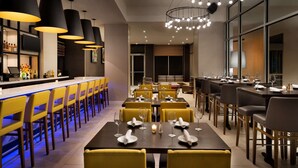 Een modern restaurant met een bar, gele stoelen en tafels gedekt voor diners.