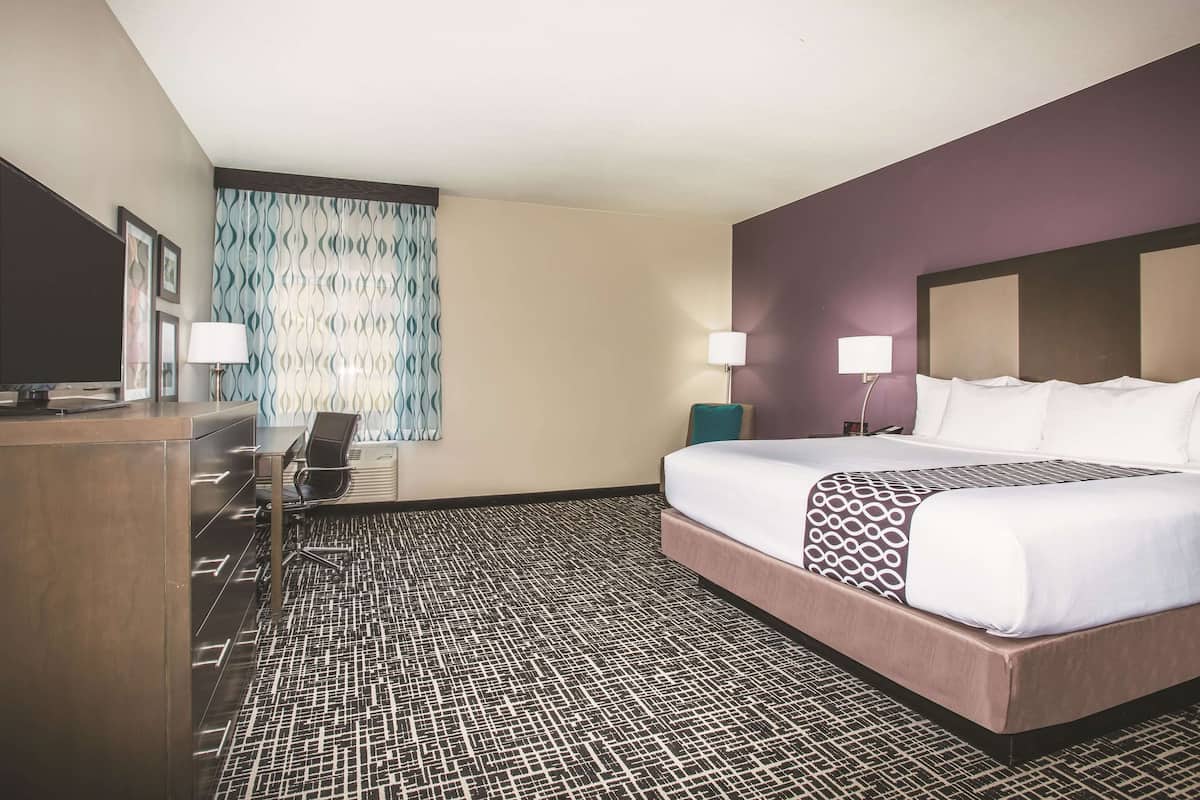 Ein Hotelzimmer mit einem großen Bett, einem Schreibtisch mit Stuhl, einem Fernseher und einem Vorhang mit Muster.