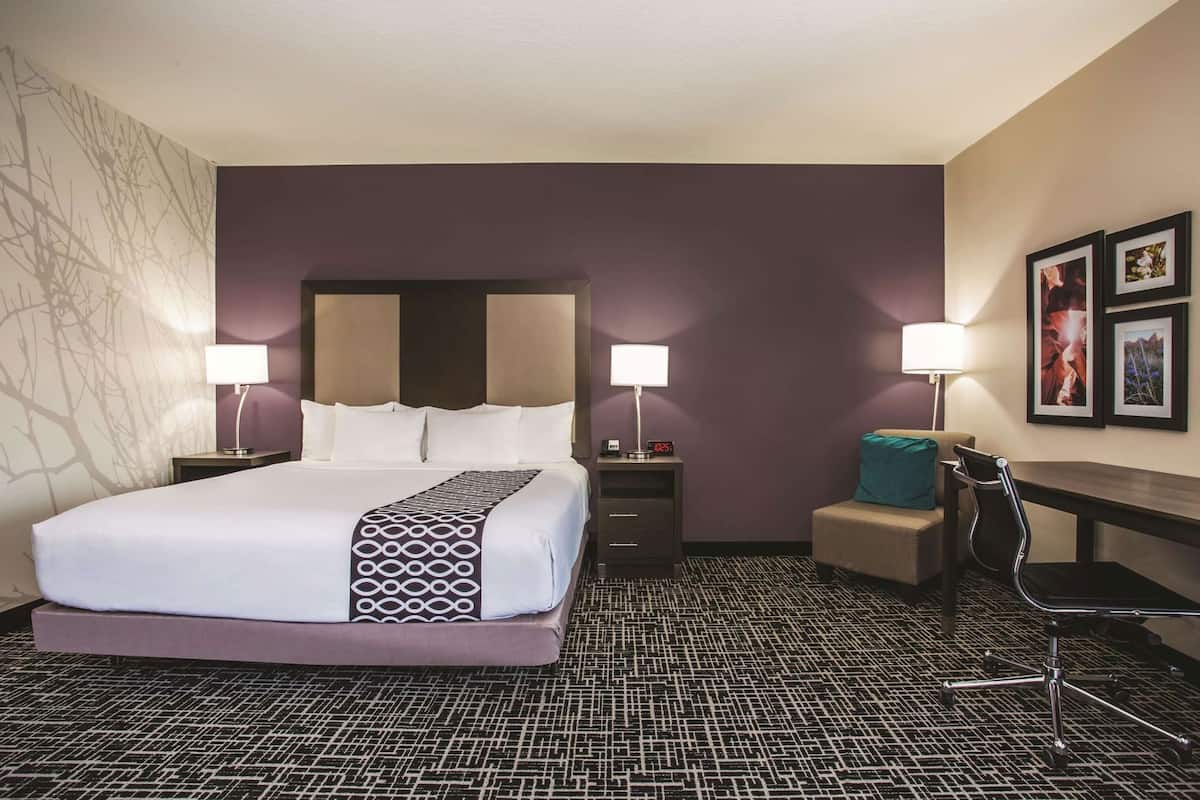 Ein Hotelzimmer mit einem großen Bett, zwei Nachttischen mit Lampen, einer kleinen Sitzecke und einer Wand mit gerahmten Bildern.