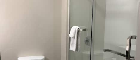 A modern bathroom with a toilet, a glass-enclosed shower, and a white towel hanging on the shower door.