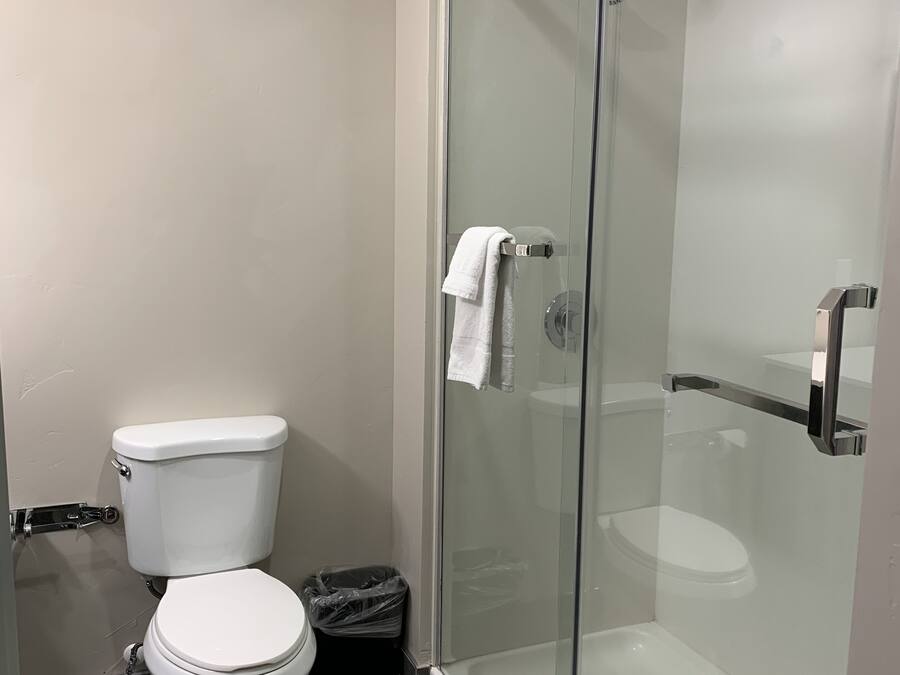 Un baño moderno con inodoro, ducha con mampara de vidrio y una toalla blanca colgada en la puerta de la ducha.
