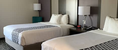 A hotel room with two beds, a nightstand, a lamp, and a digital clock.