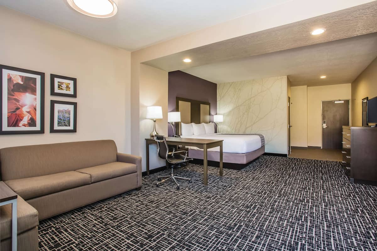 Ein Hotelzimmer mit einer Couch, einem Schreibtisch mit Stuhl, einem Bett und einem Fernseher.