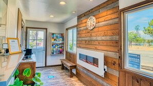 A reception area with a wooden wall, a clock, a fireplace, a bench, and a window with a view of the outside. - Ramona Valley Inn (Ramona)