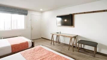 Ein Hotelzimmer mit zwei Betten, einem Schreibtisch, einer Bank, einem Fernseher und einem Fenster mit Vorhang.