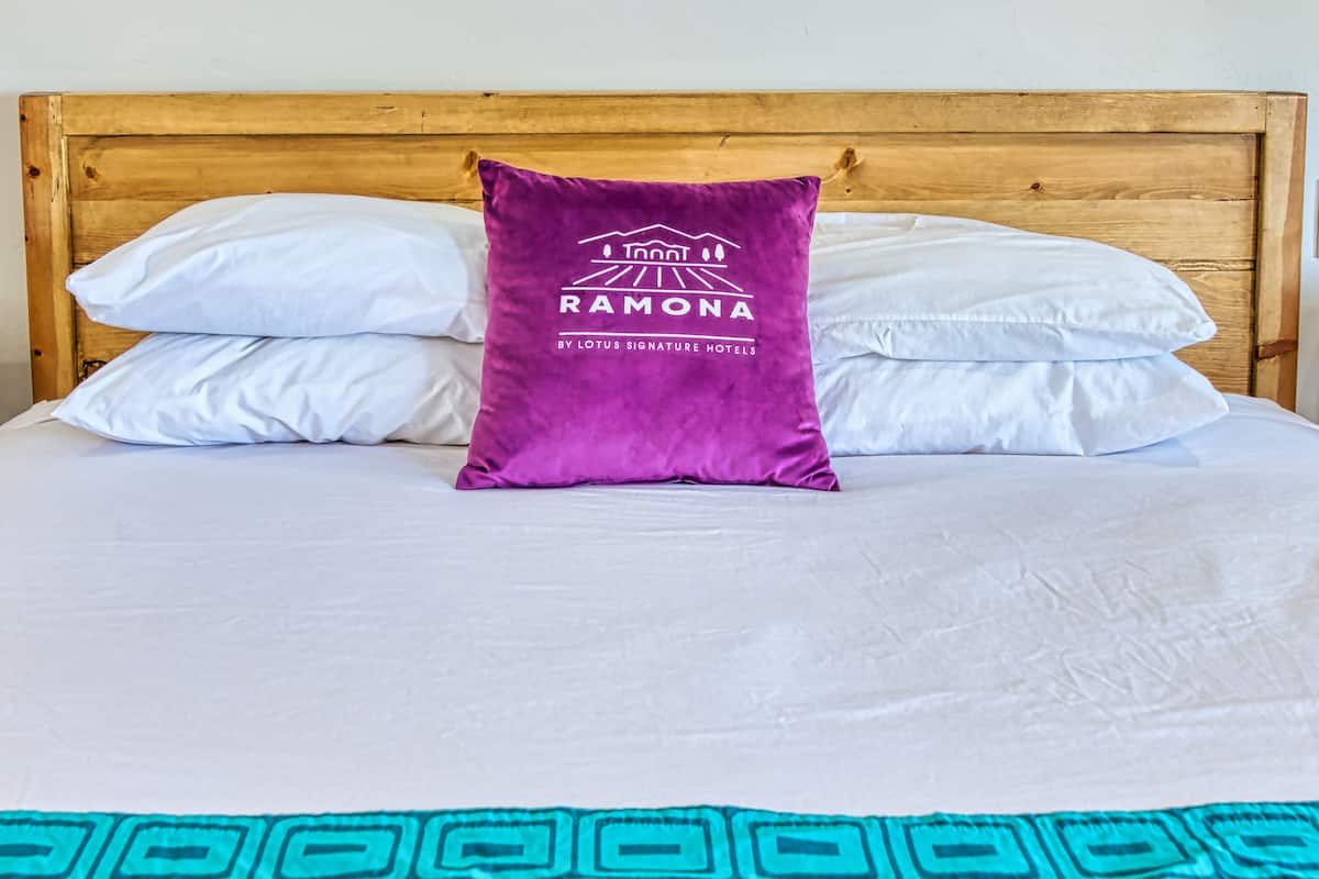 Un letto con lenzuola bianche, un cuscino viola con un logo e una coperta a motivi color acquamarina.