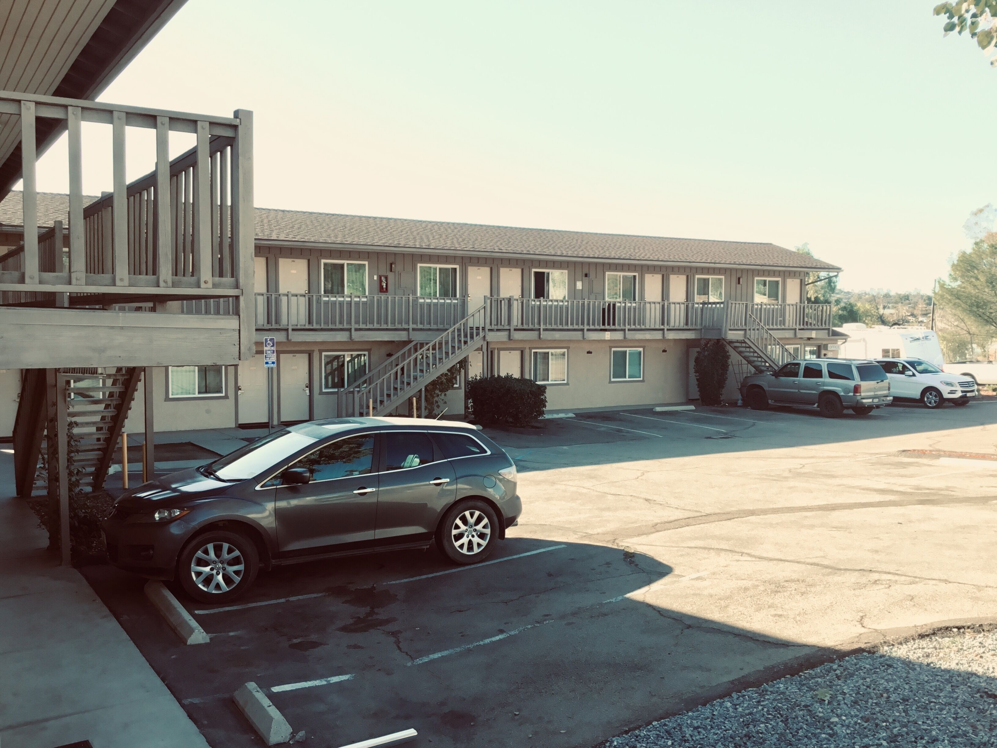 A motel with a parking lot, a staircase leading to the upper floor, and a covered outdoor area.