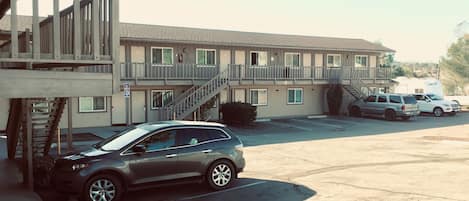 A motel with a parking lot, a staircase leading to the upper floor, and a covered outdoor area.