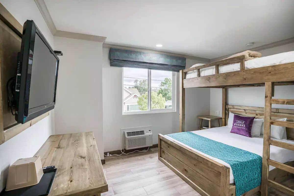 Una stanza con un letto a castello, una scrivania con un computer, una televisione e una finestra vista case.