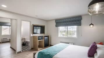 A bedroom with a bed, a desk, a television, and a window.