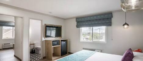 A bedroom with a bed, a desk, a television, and a window.